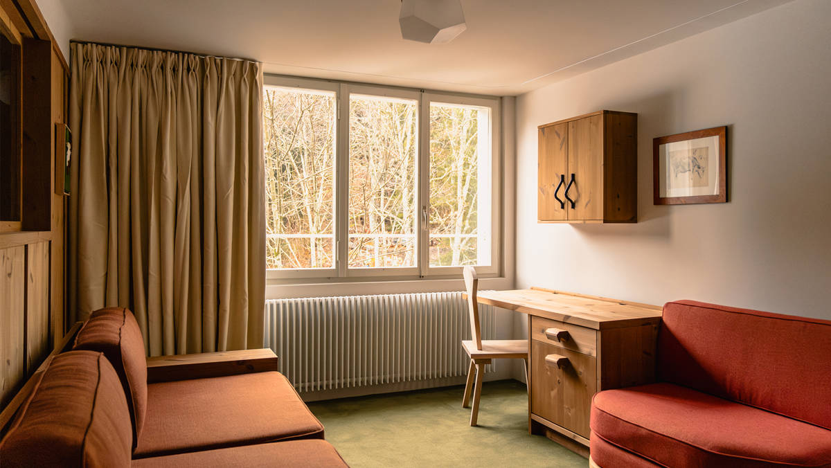 A photo of the living space features a cozy sofa set near a glass window overlooking trees.