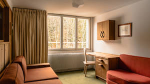 A photo of the living space features a cozy sofa set near a glass window overlooking trees.