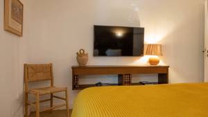 A TV is mounted on the wall above the cabinet, directly opposite the cozy bed.