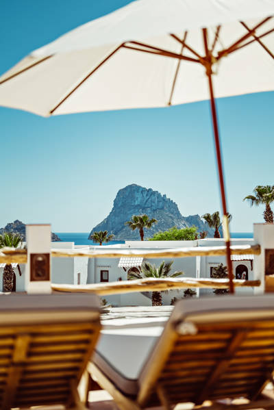 Transats sous un parasol avec vue sur la mer et l’îlot rocheux d’Ibiza