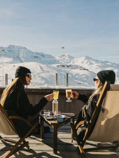 Two people on the terrace at Le Val Thorens, overlooking the slopes with a drink in hand