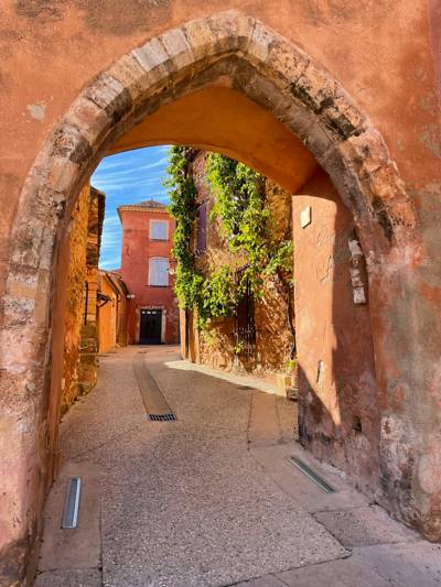 Arc en pierre ouvrant sur une ruelle aux murs ocre de Roussillon dans le Luberon
