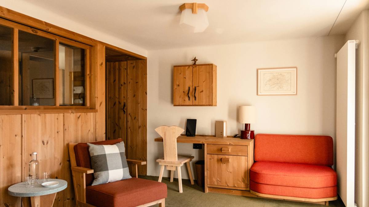 A tidy bedroom features cozy chairs placed near a table beneath the wall-mounted cupboard.