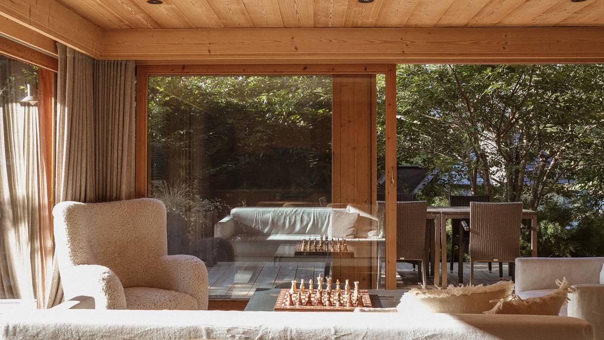 A feather-touch sofa set is placed near the large glass window overlooking lush greenery.