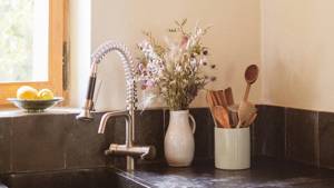 A small flower vase and crockery stand are placed on the kitchen countertop beside washbasin.