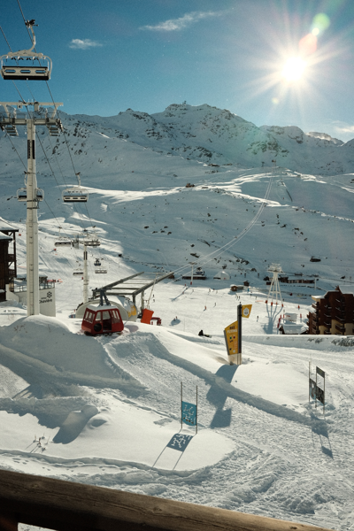 Ski slopes, chairlifts, and cable cars in the snowy resort village against rugged mountain peaks under a bright sun at Val Thorens Ski Resort.