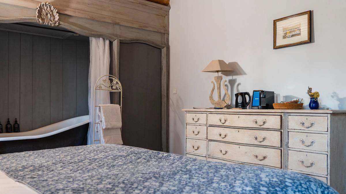 A tidy bedroom features a cozy bed, decorative items on left shelves, and a portrait above.