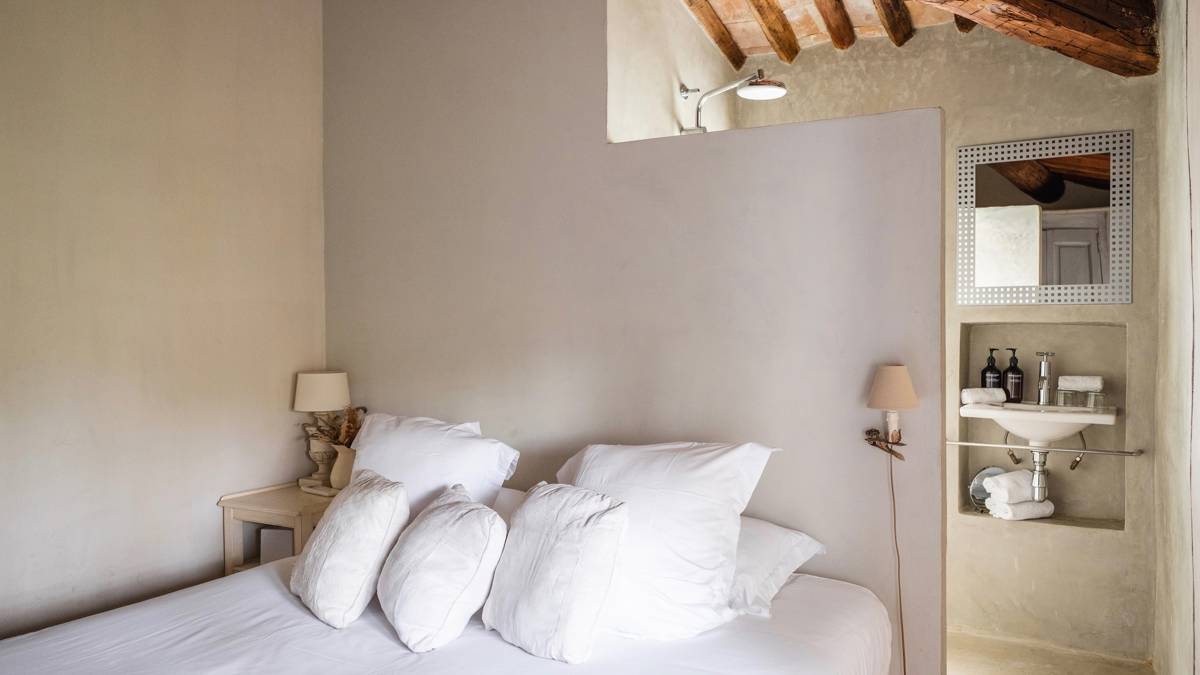 A tidy bedroom features a cozy bed, a side table with lamp, and a visible mirror.