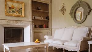 An organized living space features a cozy sofa set and a portrait above the fireplace.
