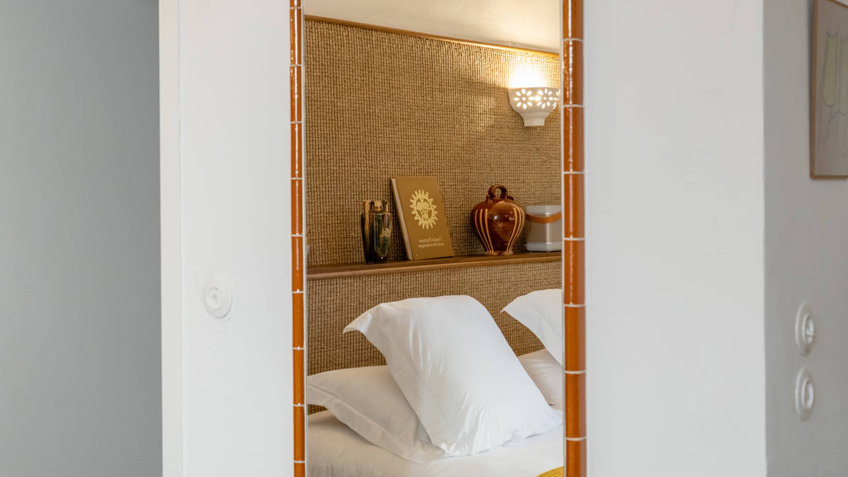 A reflection of a cozy bed with a notebook on the headboard appears in the mirror.