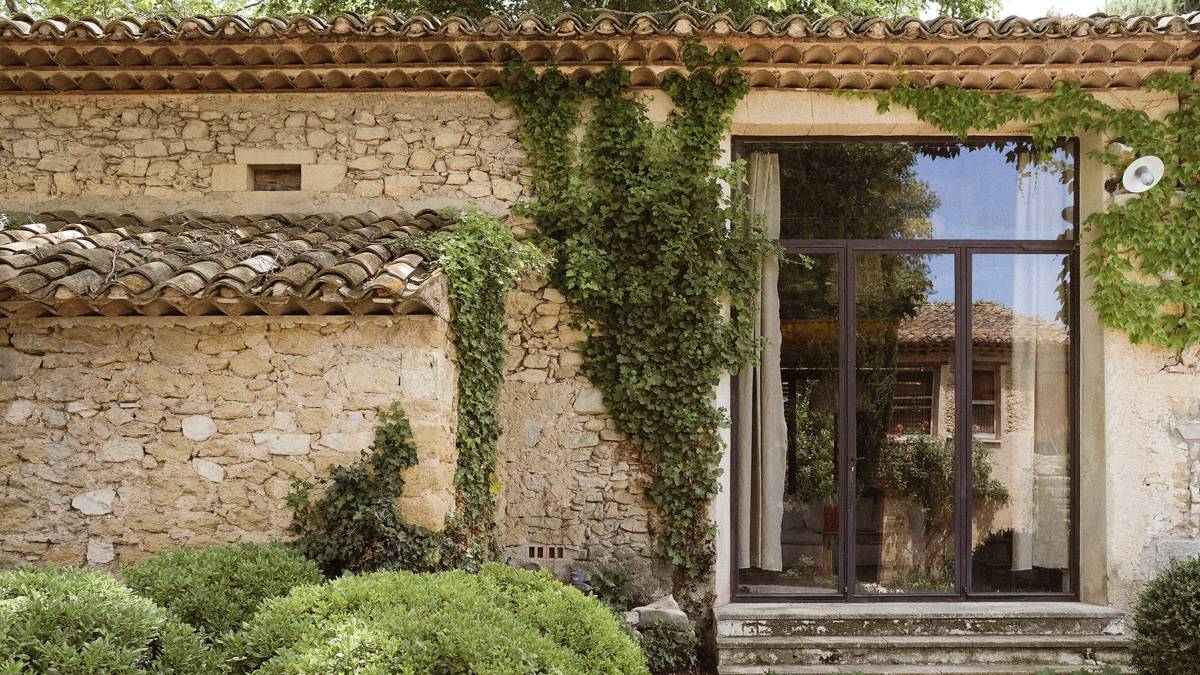 A clicked photo of the house exterior displays green lush plants near the glass door.