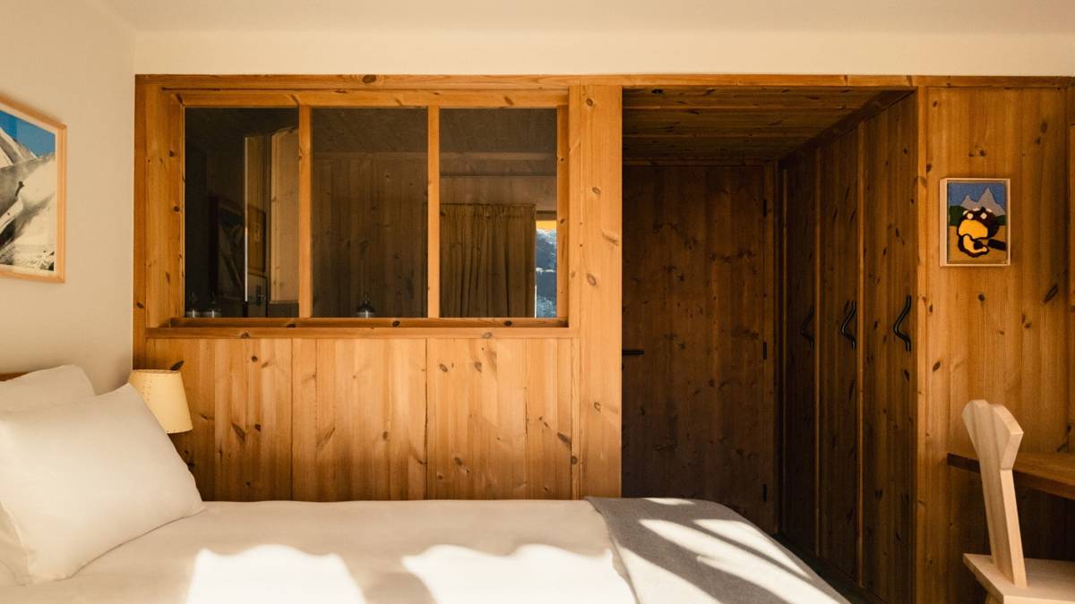 A wooden-finished wardrobe is placed in the bedroom, positioned beside a table and chair.