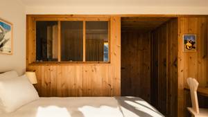 A wooden-finished wardrobe is placed in the bedroom, positioned beside a table and chair.