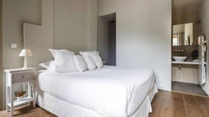 A tidy bedroom features a cozy bed, side table with lamp, and visible bathroom mirror.