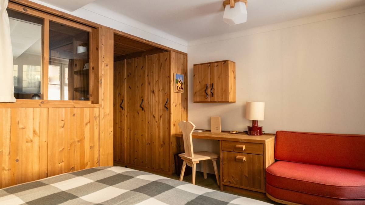 A wooden-finished wardrobe stands in the bedroom, positioned beside a table and chair.