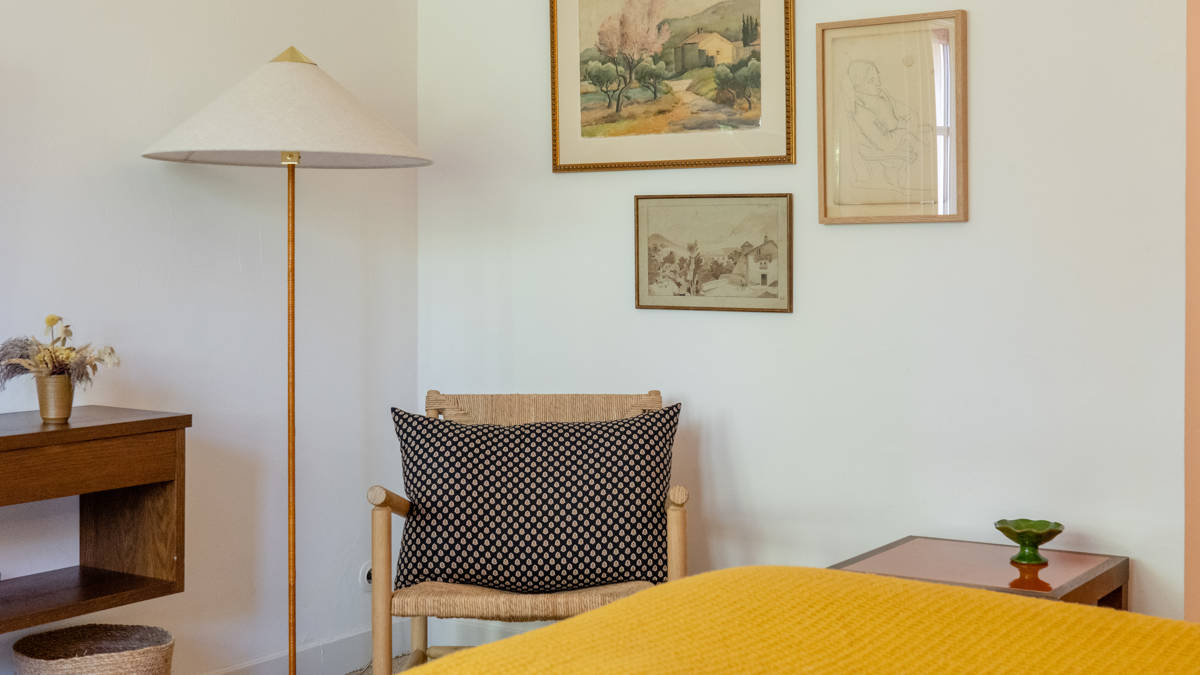 A cozy chair is placed in the corner with a stand lamp and portraits above.