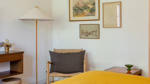 A cozy chair is placed in the corner with a stand lamp and portraits above.