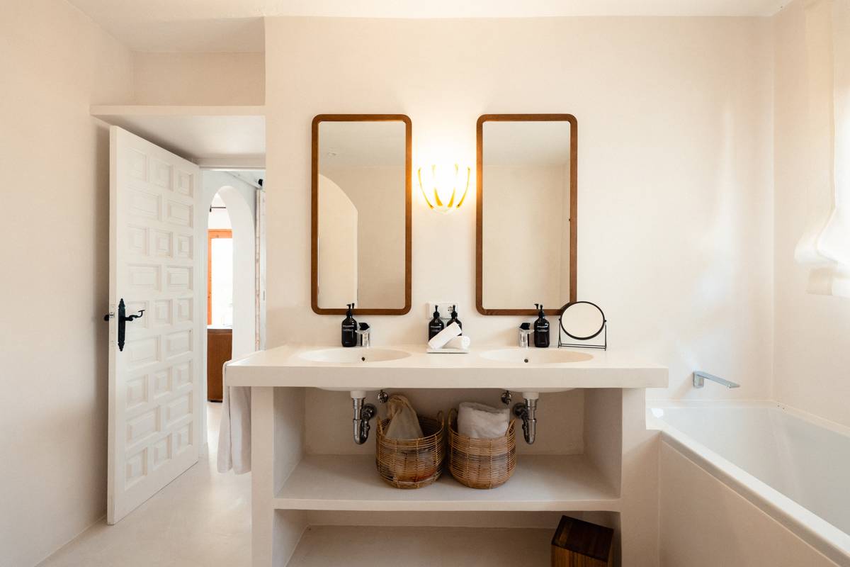 Salle de bain lumineuse avec double vasque, miroirs en bois, paniers en osier et baignoire blanche.