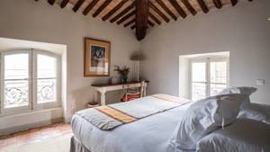 A tidy bedroom features a cozy bed, a table in front, and a portrait above.