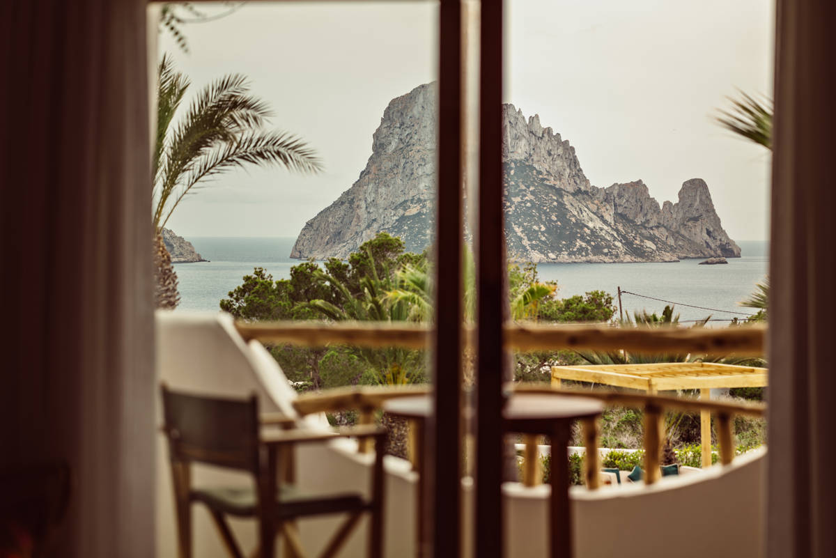 Vue depuis la chambre de deux transats sur terrasse surplombant l'océan et île rocheuse sous ciel.
