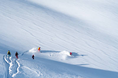 A group of skiers carving fresh tracks through deep powder snow on a vast, sunlit mountain slope at Val Thorens Ski Resort.