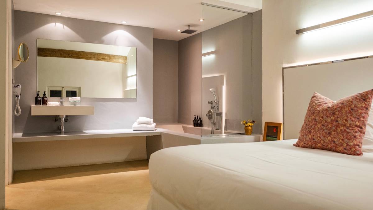 A properly arranged bedroom featuring a cozy bed and a wall basin with large mirror.