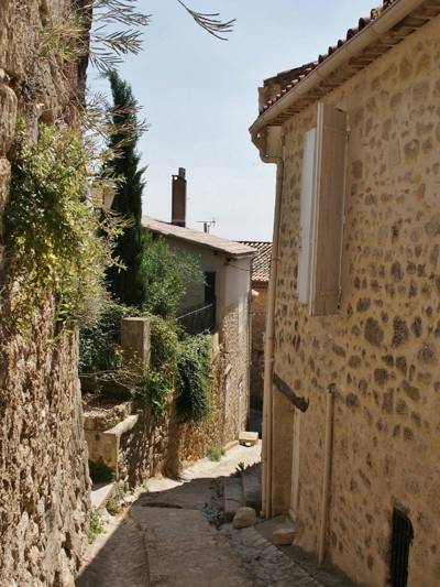 Ruelle pavée de Ménerbes dans le Luberon, bordée de murs en pierre calcaire et de végétation méditerranéenne