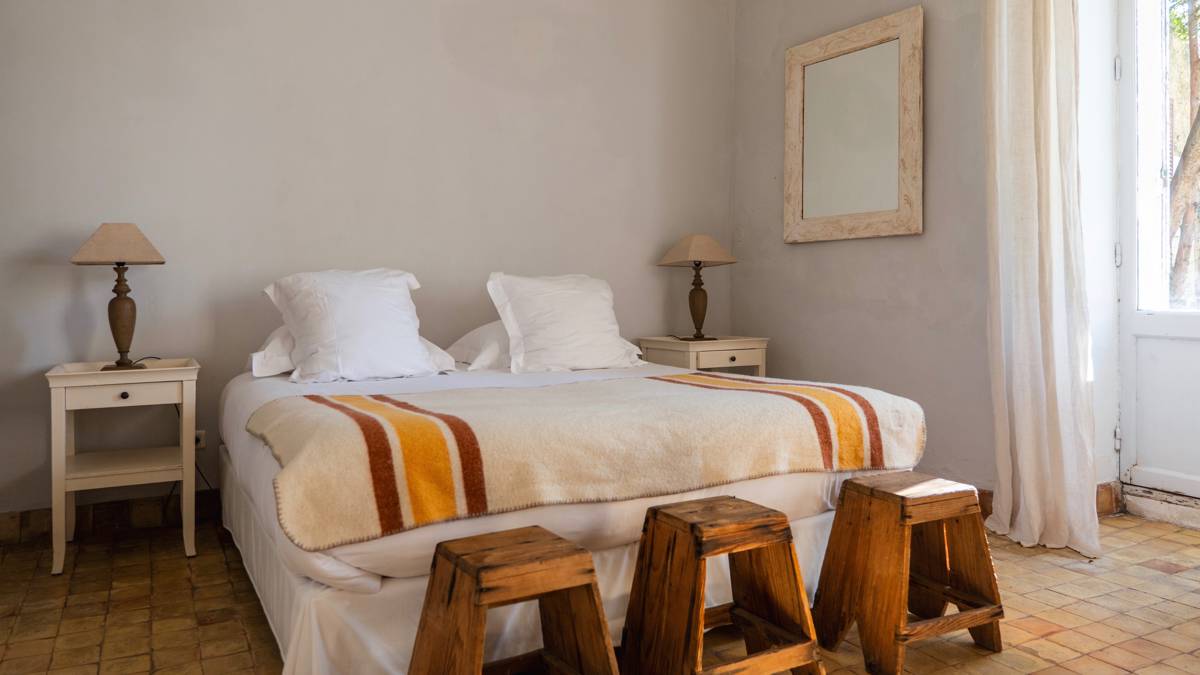 A tidy bedroom featuring a cozy bed, two side tables with lamps, and three chairs.