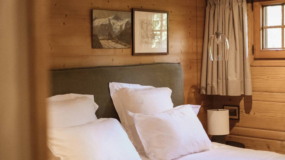 A cozy bed is placed by the wooden-finished wall with two portraits mounted above.