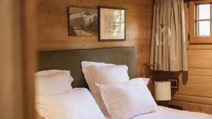 A cozy bed is placed by the wooden-finished wall with two portraits mounted above.