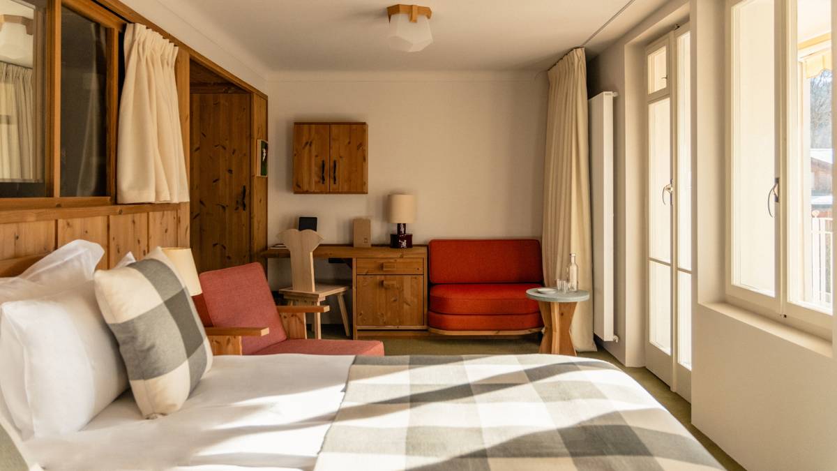 A tidy bedroom features a cozy bed and chairs near a table under the wall-mounted cupboard.