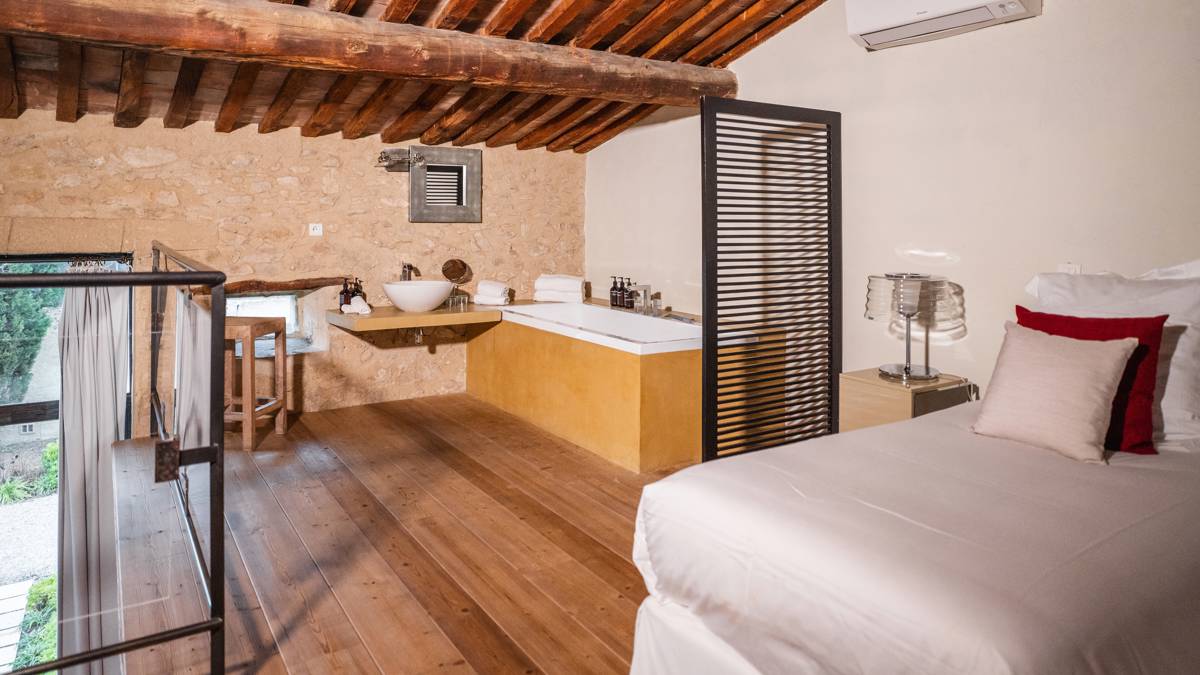 A cozy bed, corner bathtub, mounted washbasin, and nearby chair create organized comfort.