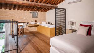 A cozy bed, corner bathtub, mounted washbasin, and nearby chair create organized comfort.