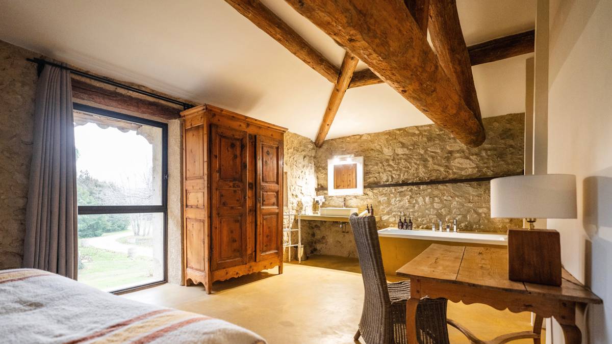 Properly arranged bedroom with cozy bed, table and chair, and wooden cupboard near glass door.