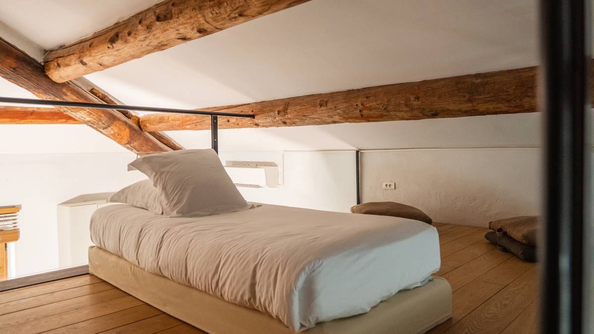 A cozy bed is placed upstairs with two small sitting bags to its right.