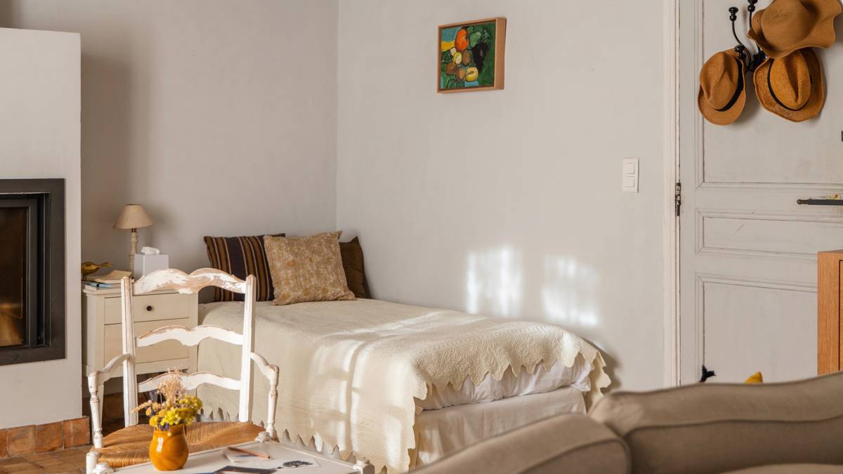 A tidy bedroom features a cozy bed, a nearby chair, and a portrait above.