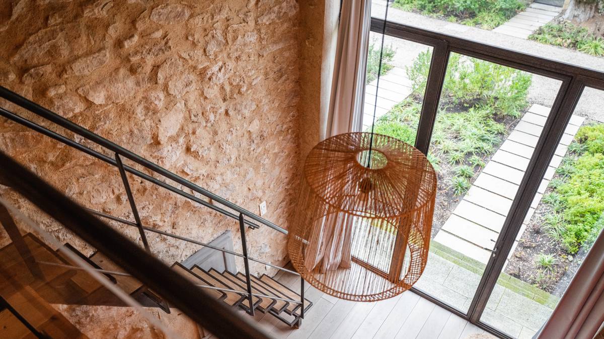An aerial photo of the stair room showcases stairs, a hanging chandelier, and glass window view.