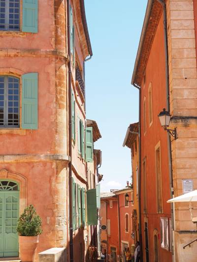 Ruelle du village de Roussillon dans le Luberon, aux façades ocre et terracotta baignées de lumière provençale sous un ciel bleu éclatant