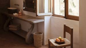 A round wash basin on a uniquely designed table and a chair with fruit bowl.