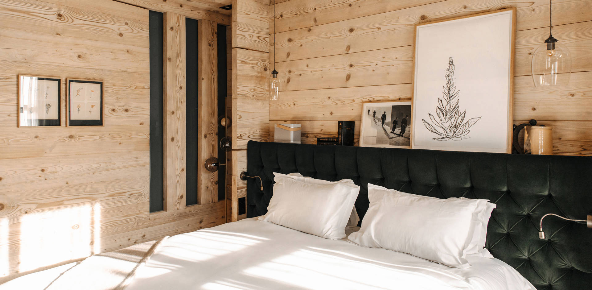 A dark green cozy bed is placed against a wooden-finished wall with two portraits above.