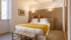A well-organized bedroom features a cozy bed with a portrait mounted on the left wall.
