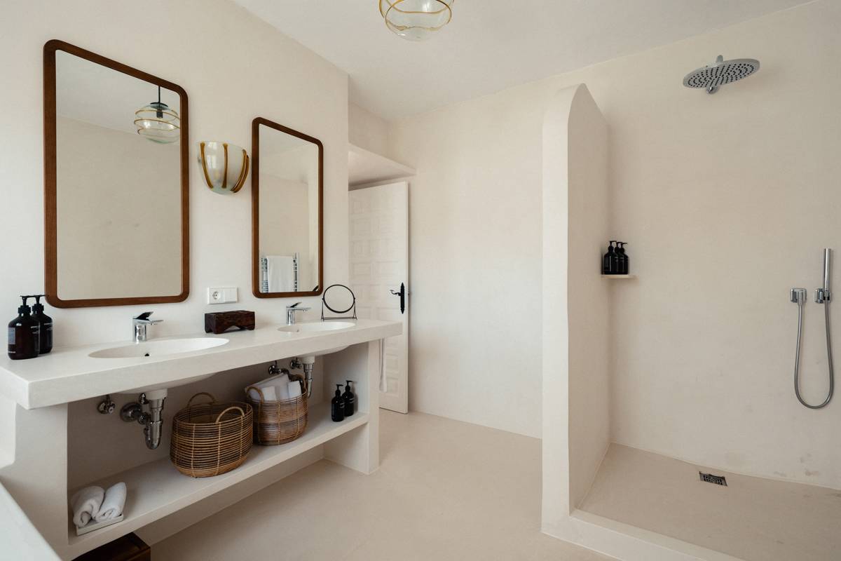 Salle de bain minimaliste avec double vasque, grands miroirs, douche à l’italienne, paniers en osier, tons beiges.