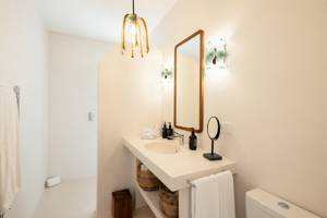 Salle de bain lumineuse avec un lavabo moderne, un miroir en bois, une suspension en verre, des paniers en osier et une décoration minimaliste dans des tons neutres.