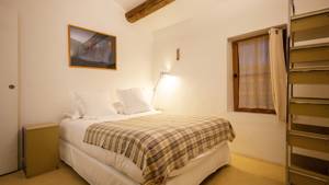 A tidy bedroom features a cozy bed with a rectangular portrait mounted above on wall.