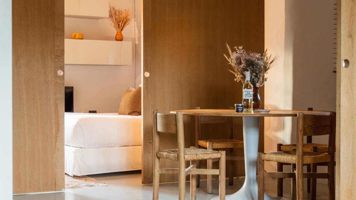 A well-organized dining area features a round table with chairs, flower vase, and wine bottle.