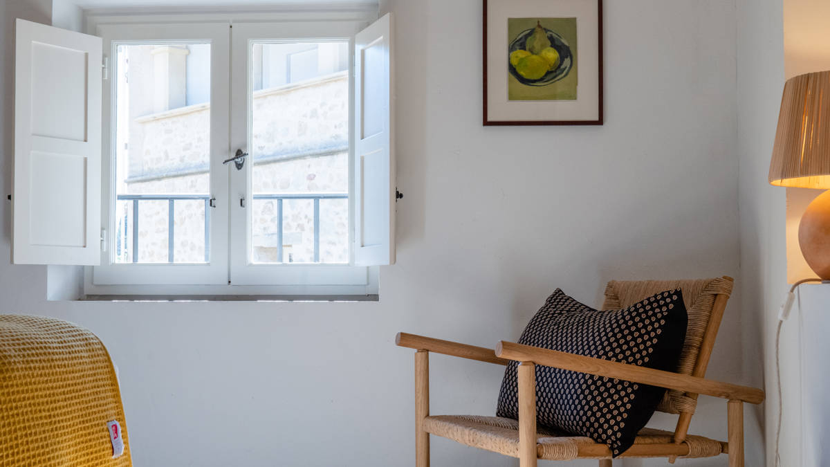 A cozy chair is placed near the glass window with a portrait mounted above.