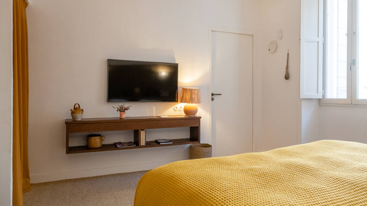 A TV is mounted on the wall above the cabinet, directly facing the cozy bed.