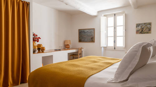 A properly organized bedroom features a cozy bed, a chair by the table, and a portrait above.