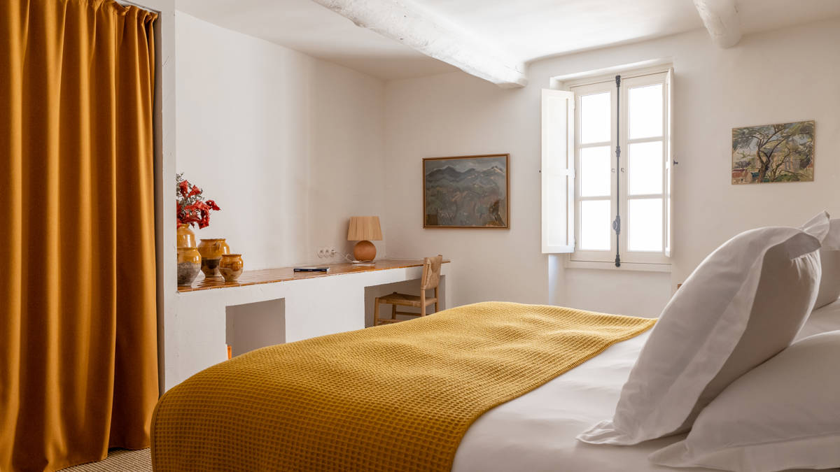 A properly organized bedroom features a cozy bed, a chair by the table, and a portrait above.