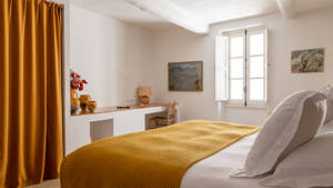 A properly organized bedroom features a cozy bed, a chair by the table, and a portrait above.